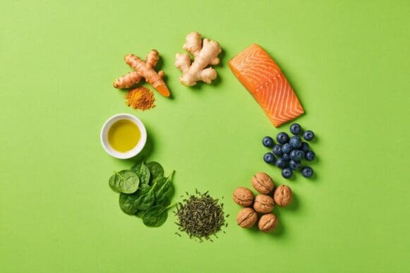 Alimentos anti-inflamatórios — cúrcuma, gengibre, salmão, mirtilo, nozes, chá verde, espinafre e azeite — sobre fundo verde-limão