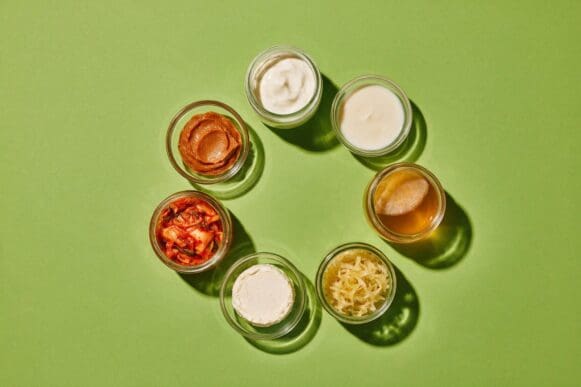 Iogurte natural, kefir, kombucha, chucrute, kimchi e missô em potinhos de vidro sobre fundo verde-limão