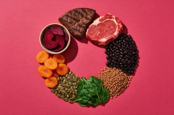Alimentos ricos em ferro — fígado, carne vermelha magra, feijão preto, lentilha, espinafre, sementes de abóbora, damasco seco e beterraba — sobre fundo rosa