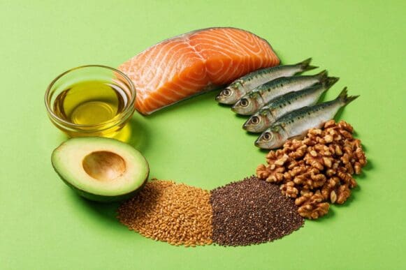 Alimentos ricos em ômega 3 — salmão, sardinha, nozes, chia, linhaça, abacate e azeite — dispostos em círculo sobre fundo verde-limão