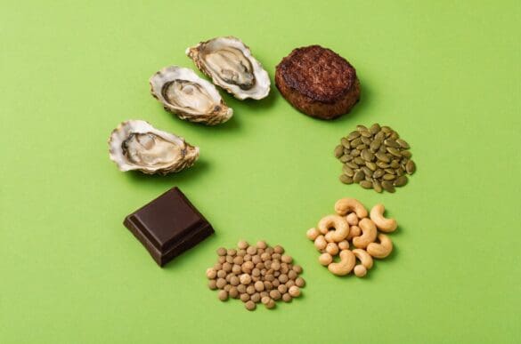 Alimentos ricos em zinco — ostras, carne bovina, sementes de abóbora, castanhas, grão-de-bico, chocolate amargo e lentilha — sobre fundo verde-limão