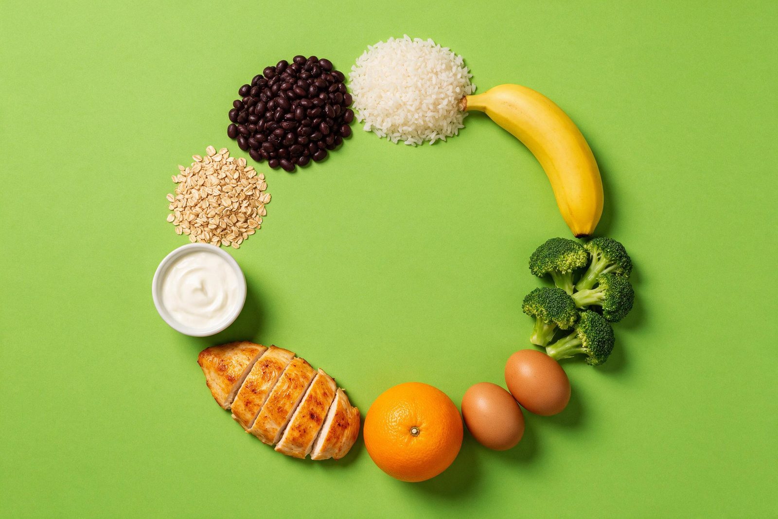 Alimentos do dia a dia — feijão, arroz, banana, brócolis, ovos, laranja, frango e aveia — dispostos em círculo sobre fundo verde-limão