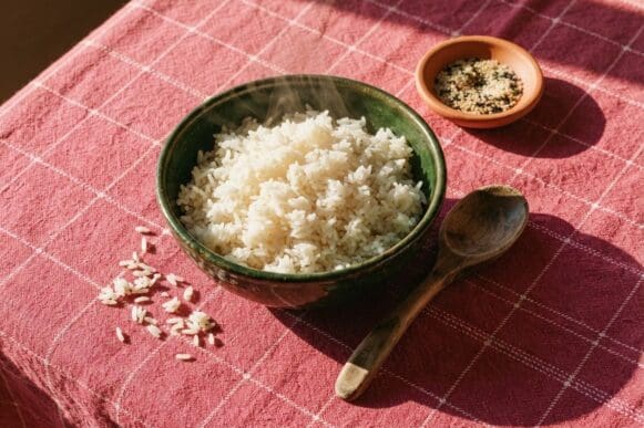 Tigela verde-escura de arroz jasmim soltinho com vapor subindo, sobre toalha rosa da Frutifica