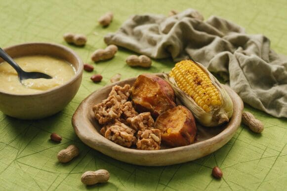 Comidas de festa junina — curau de milho, milho na espiga, batata-doce, amendoim e pé-de-moleque — sobre toalha verde-limão