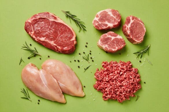 Cortes crus de patinho, lombo suíno, peito de frango e carne moída dispostos em círculo sobre fundo verde-limão