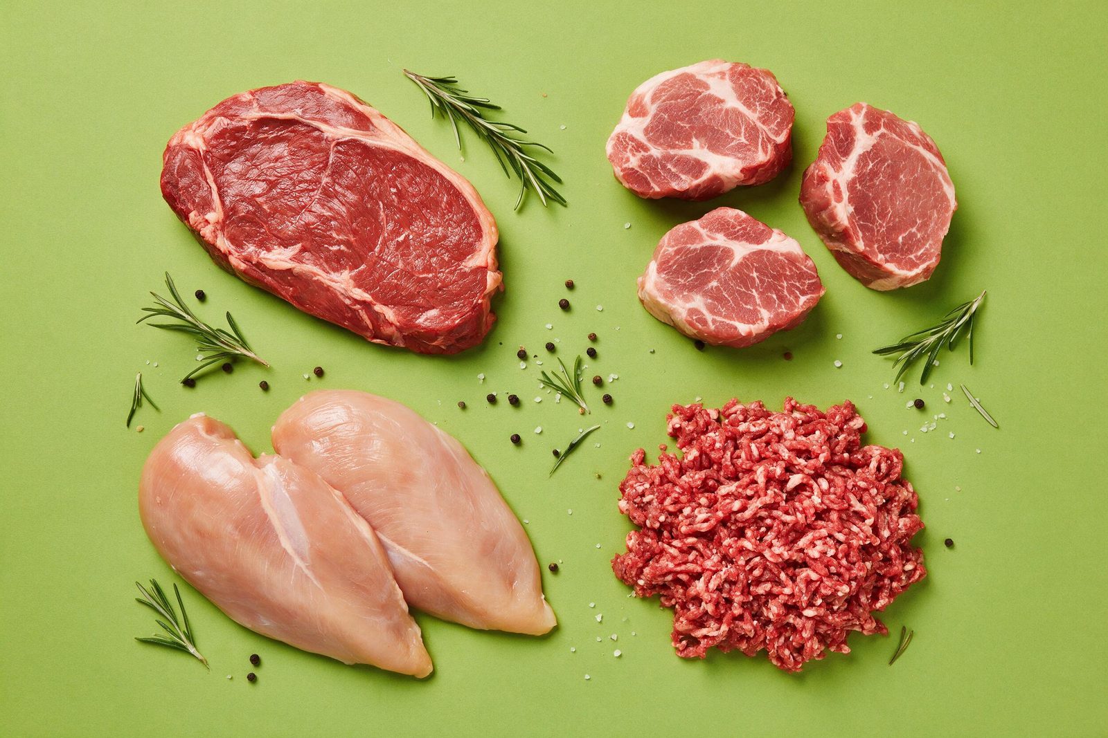 Cortes crus de patinho, lombo suíno, peito de frango e carne moída dispostos em círculo sobre fundo verde-limão