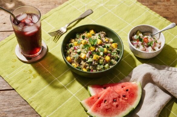 Comidas leves de verão — salada de quinoa com manga, melancia gelada e chá de hibisco com gelo — sobre toalha verde-limão