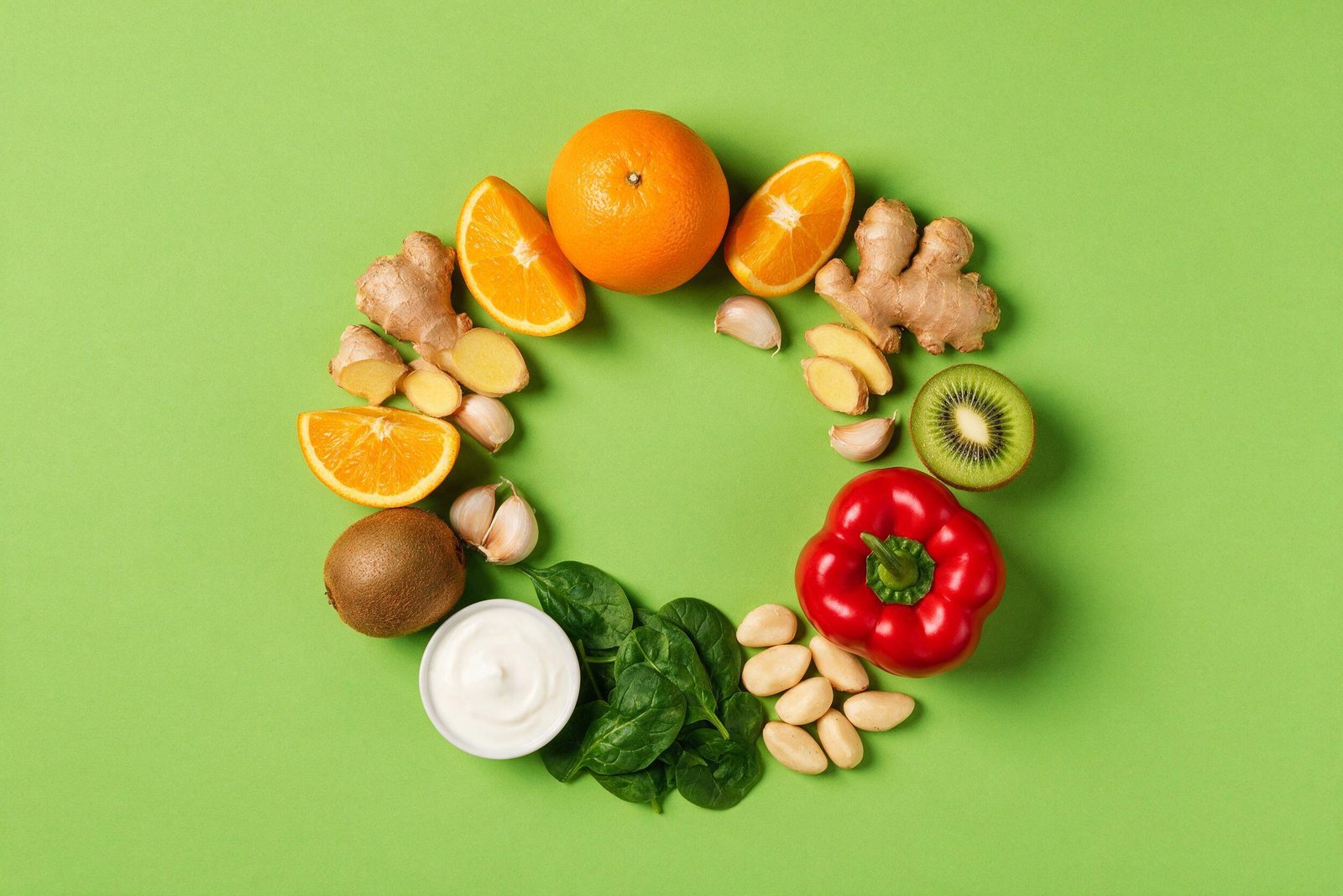 Alimentos que ajudam a imunidade — laranja, gengibre, alho, kiwi, pimentão, espinafre, iogurte e castanha-do-pará — sobre fundo verde-limão