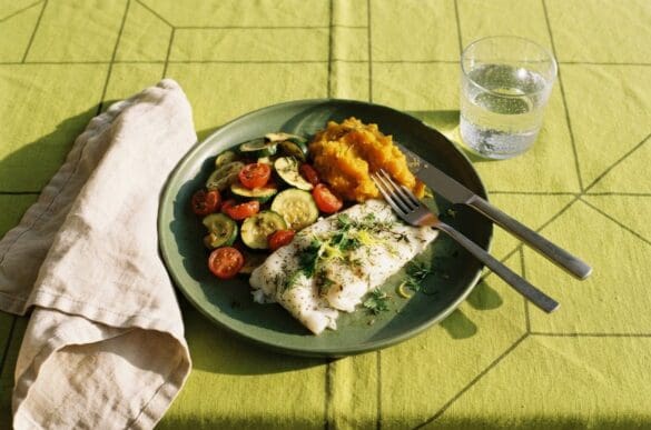 Jantar leve com peixe assado, abobrinha refogada e purê de abóbora em prato verde sobre toalha verde-limão