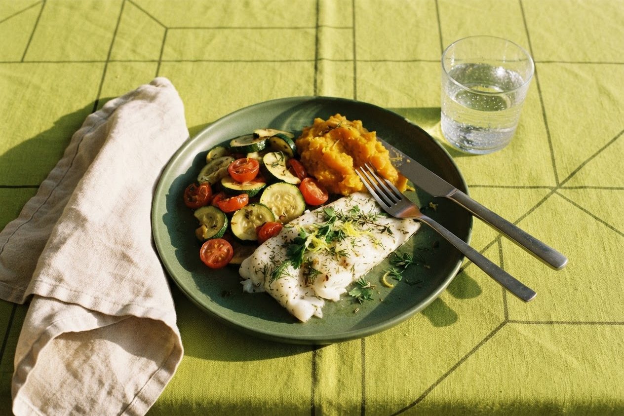 Jantar leve com peixe assado, abobrinha refogada e purê de abóbora em prato verde sobre toalha verde-limão