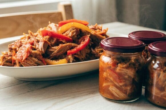 carne louca desfiada em molho de tomate e pimentão numa travessa, ao lado de potes porcionados para congelar