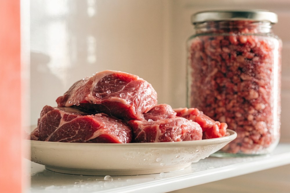 Bifes bovinos porcionados descongelando em prato fundo dentro da geladeira, ao lado de pote com carne moída