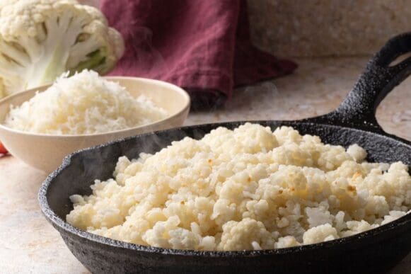 arroz de couve-flor salteado e soltinho em frigideira, ao lado de couve-flor crua ralada em tigela
