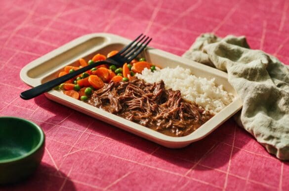 Bandeja com carne desfiada ao molho, arroz branco e cenoura com ervilha sobre toalha rosa da Frutifica