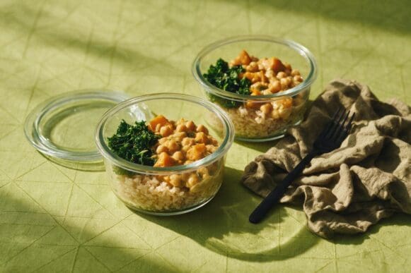 Potes de vidro com marmita vegetariana de grão-de-bico com abóbora, arroz integral e couve refogada sobre toalha verde-limão