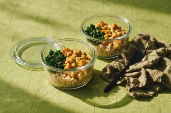 Potes de vidro com marmita vegetariana de grão-de-bico com abóbora, arroz integral e couve refogada sobre toalha verde-limão