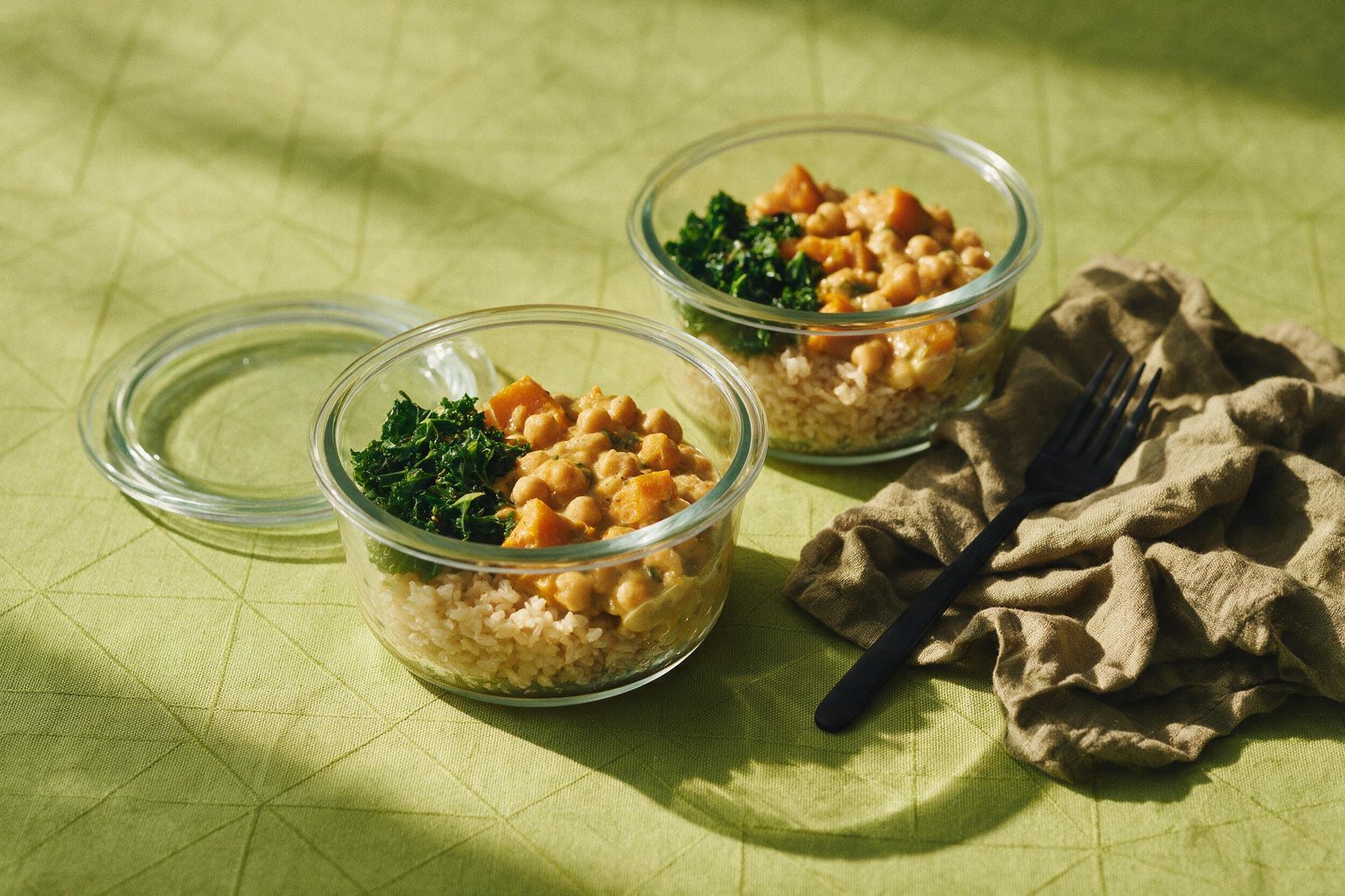 Potes de vidro com marmita vegetariana de grão-de-bico com abóbora, arroz integral e couve refogada sobre toalha verde-limão