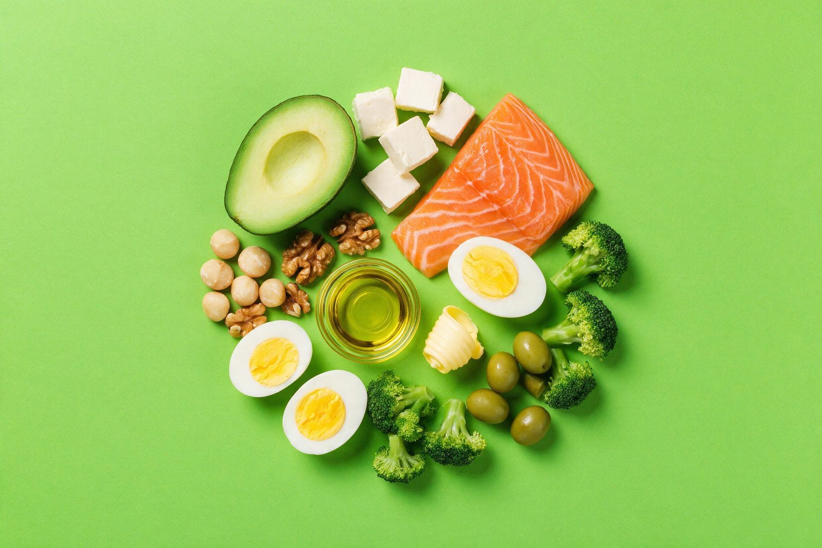 Alimentos da dieta cetogênica — abacate, salmão, queijo, castanhas, ovos, azeite e brócolis — dispostos em círculo sobre fundo rosa