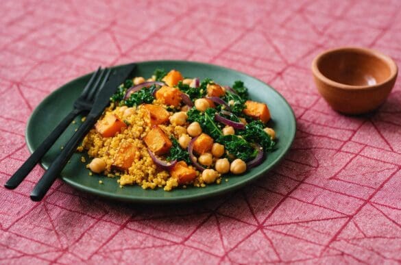 Prato verde com quinoa, abóbora assada, grão-de-bico e couve refogada sobre toalha rosa