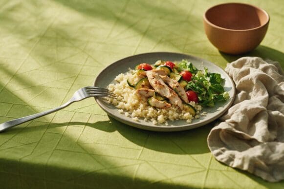 Prato verde com arroz de couve-flor, tiras de frango grelhado, abobrinha e tomate-cereja sobre toalha verde-limão