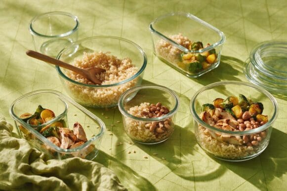 Sessão de meal prep com potes de vidro sendo montados com arroz, frango e legumes sobre toalha verde-limão da Frutifica