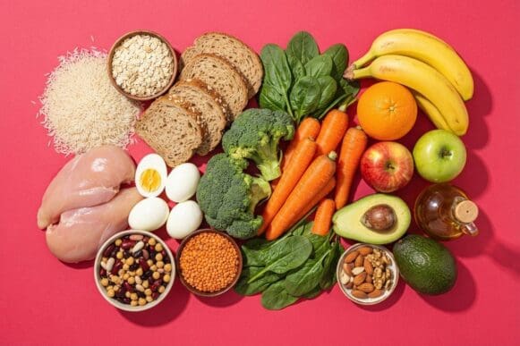 Os grupos alimentares reunidos — cereais, proteínas, legumes, frutas e gorduras boas — sobre fundo rosa