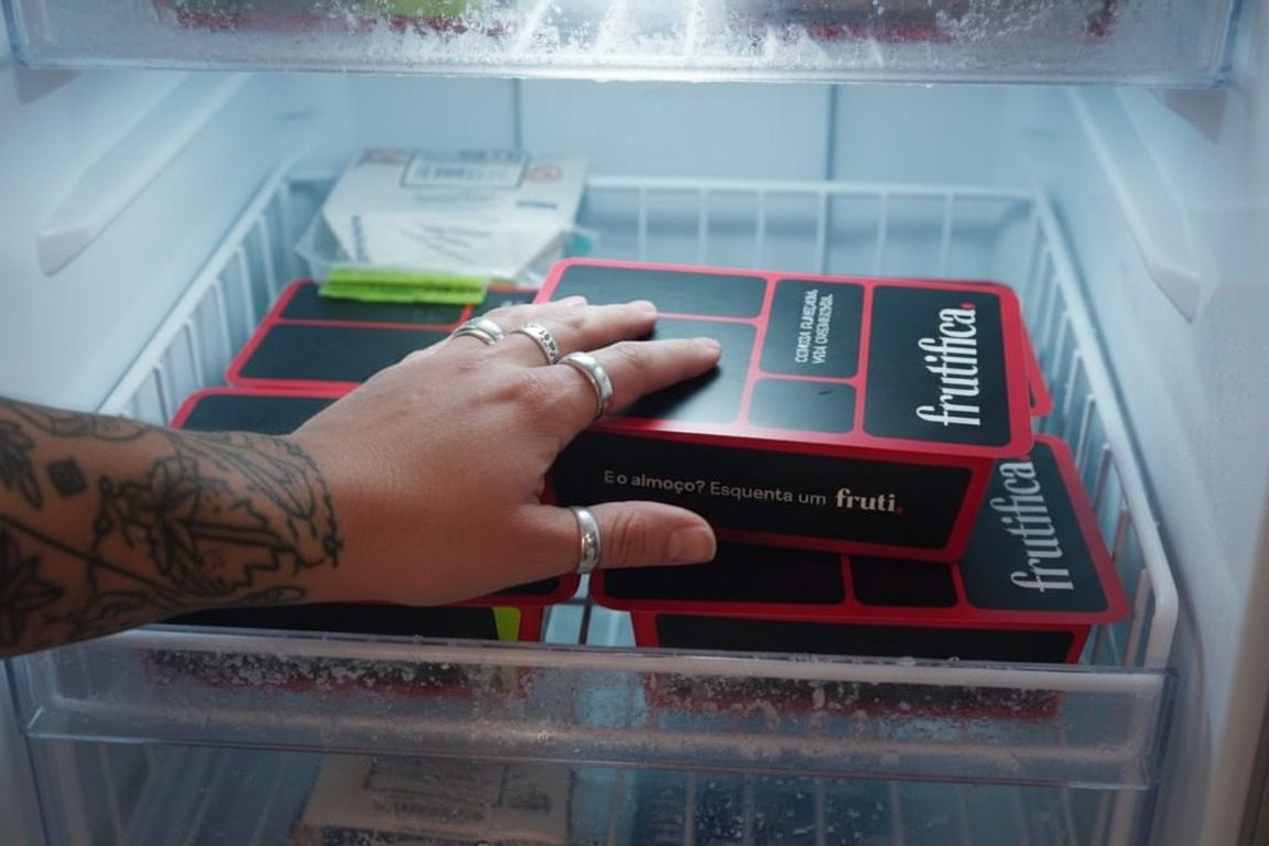 Mão retirando uma marmita da Frutifica de uma gaveta de freezer cheia de marmitas empilhadas
