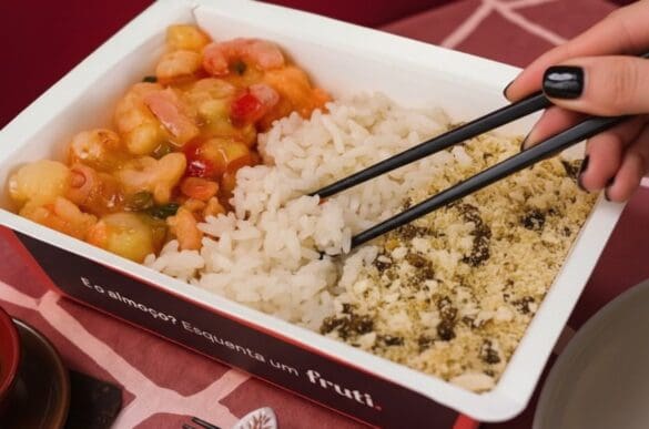 Marmita da Frutifica com arroz branco, farofa e camarão ao molho vista de cima, com hashi na mão